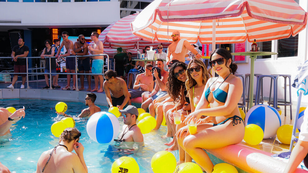 a group of people in a pool with yellow and blue balloons and umbrellas