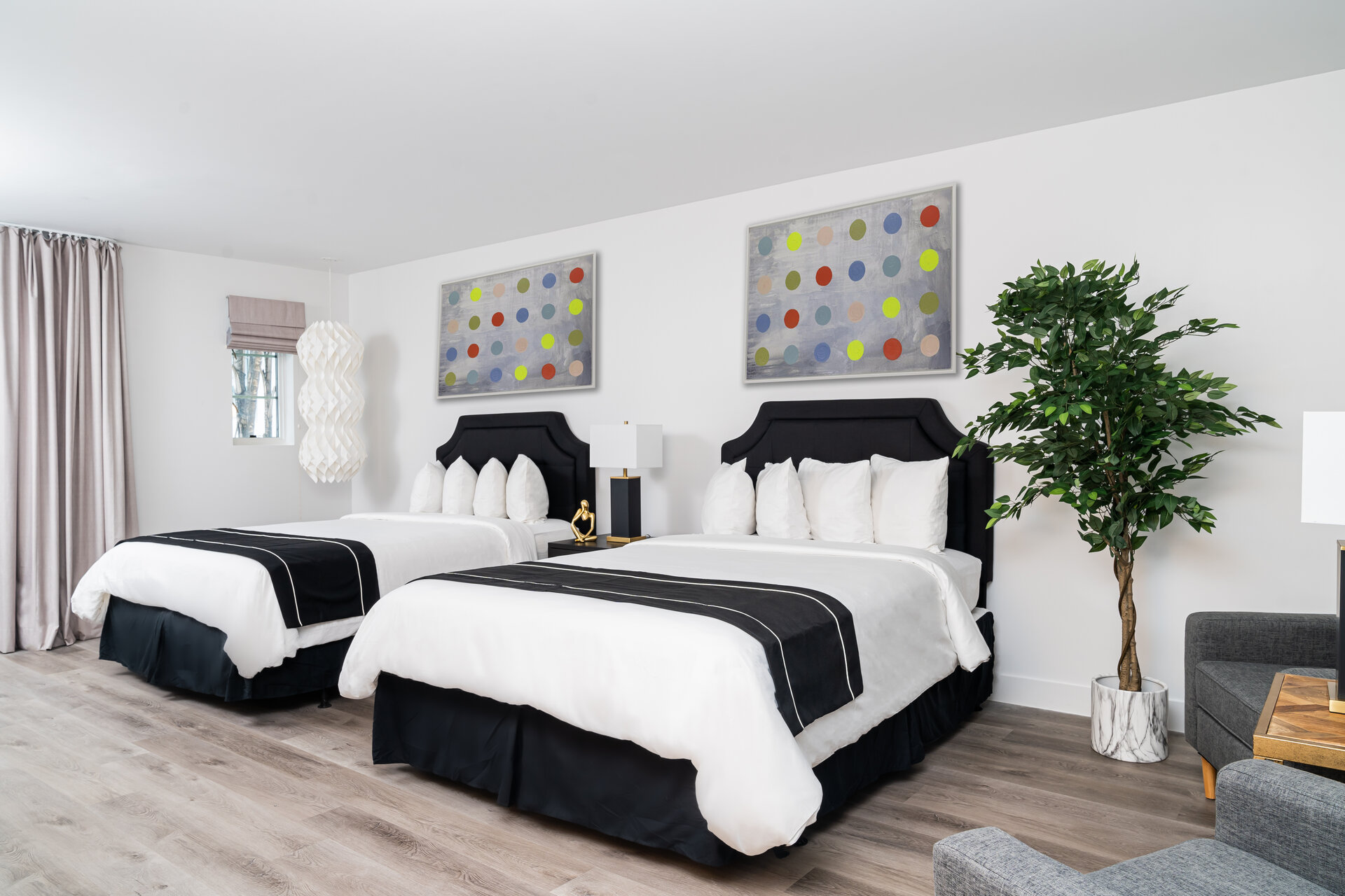 A clean and modern hotel room with two twin beds, artwork, a plant, and a sofa.