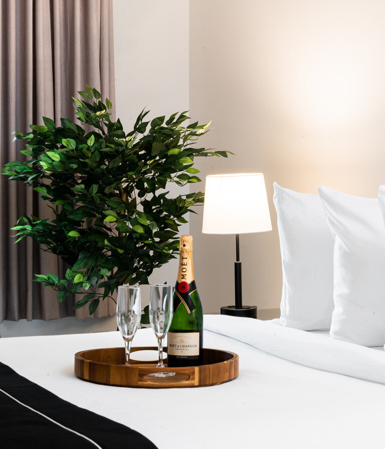 A bottle of champagne and two glasses on a wooden tray on a bed