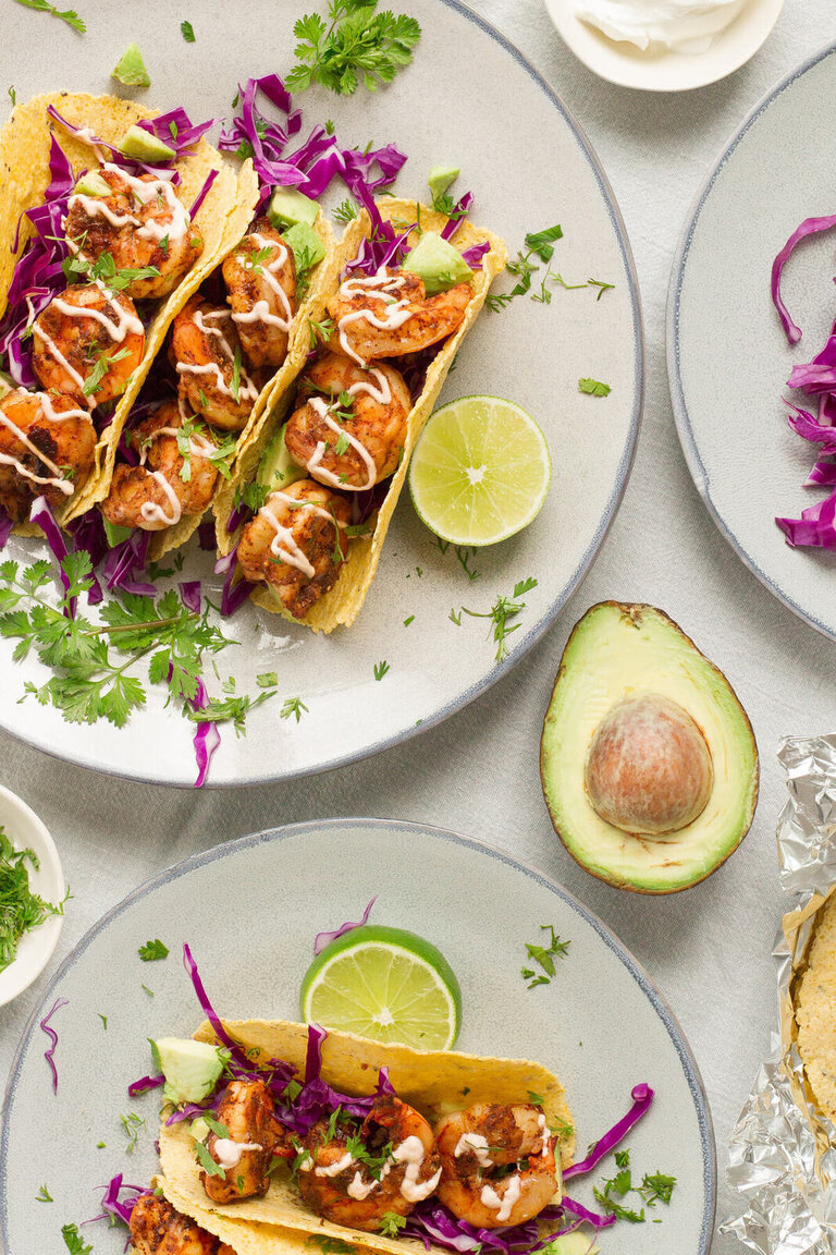 a plate of tacos with shrimp, avocado, and lime