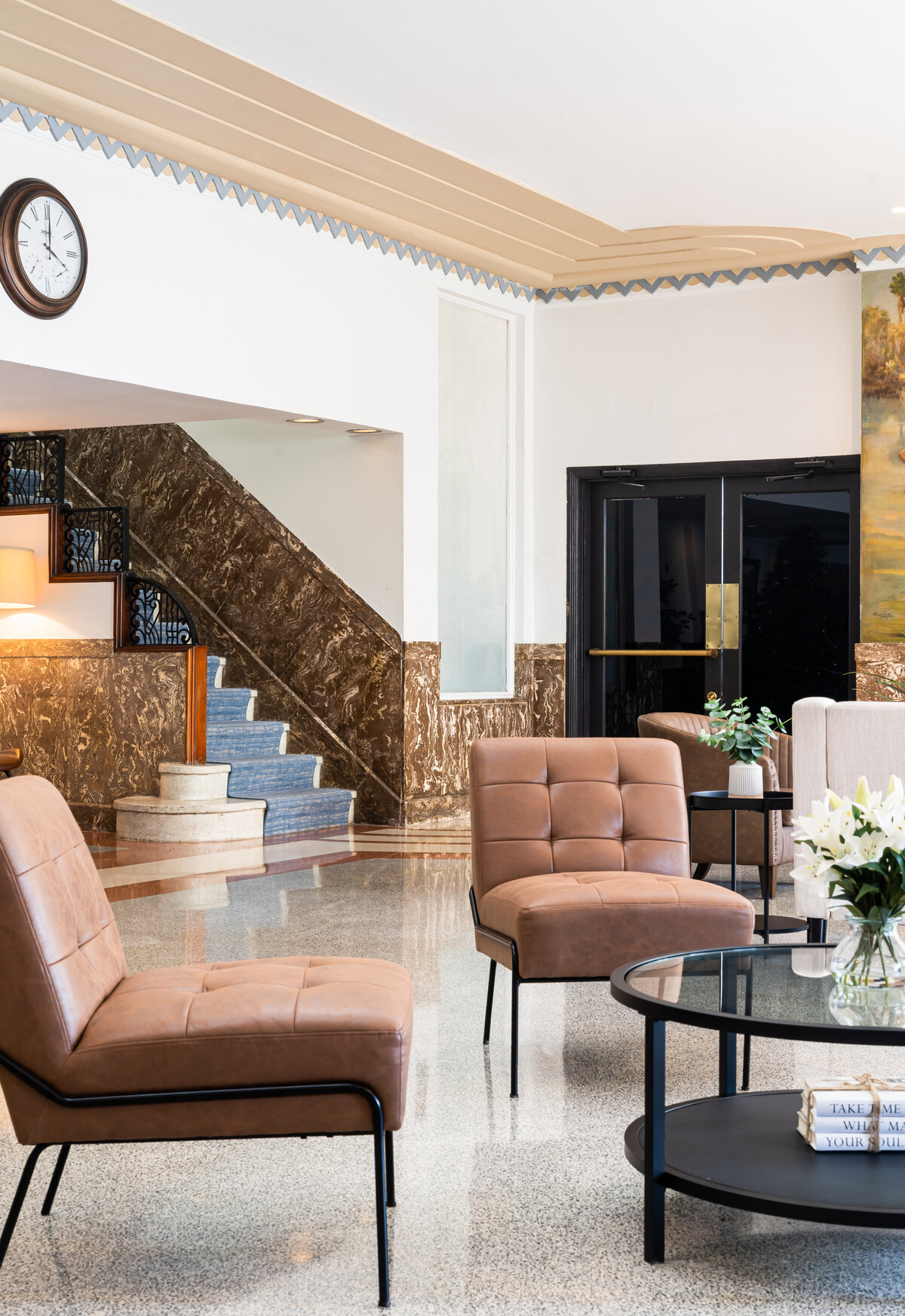 A lobby with a marble staircase, leather chairs, and a glass coffee table.