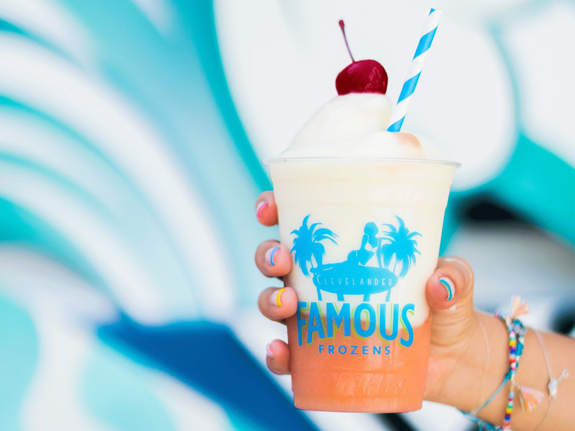 a hand holding a colorful drink with ice cream and a cherry on top