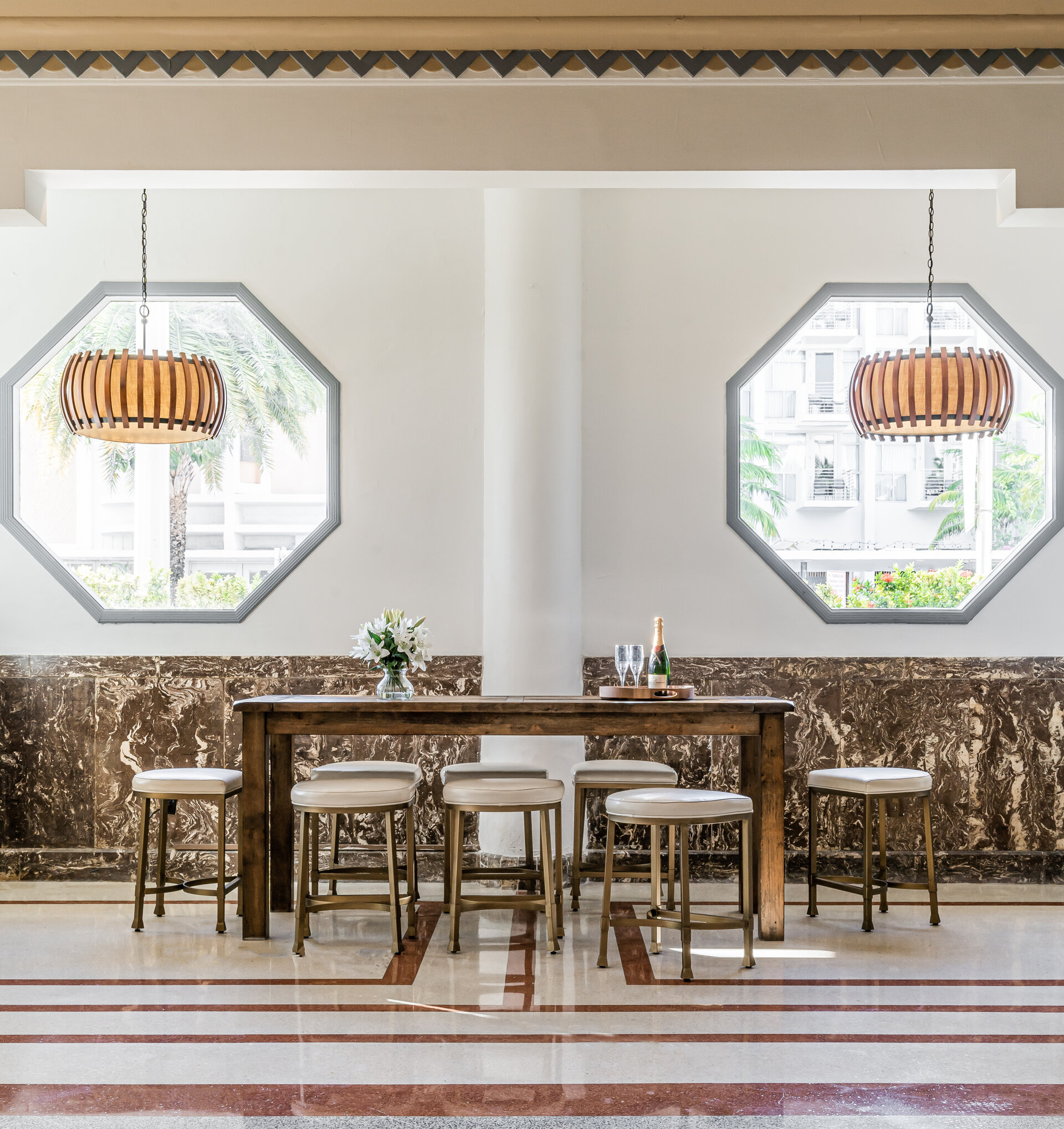 A luxurious lobby lounge with a large table and chairs, octagonal windows, and decorative lighting.